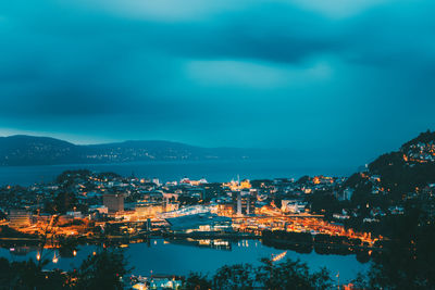 High angle view of illuminated city by sea against sky