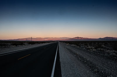 Empty road along landscape at sunset