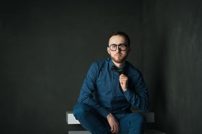 Portrait of young man sitting on steps by wall