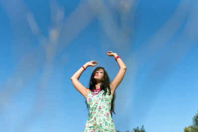 Low angle view of woman with arms raised standing against blue sky