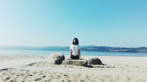 Rear view of woman sitting on beach against clear sky