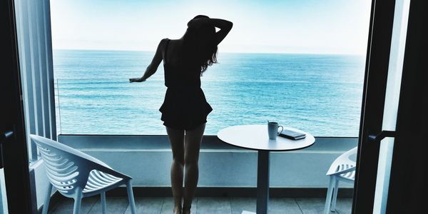 Woman standing on table by sea against sky