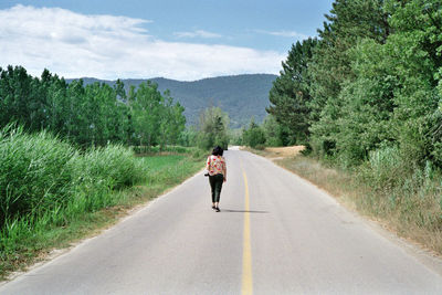 Rear view of woman walking on road amidst trees