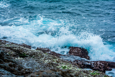 High angle view of waves splashing on rocks at shore
