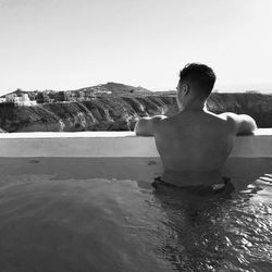 Rear view of shirtless man in infinity pool against clear sky