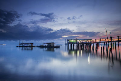 Stilt houses and pier at lake against cloudy sky