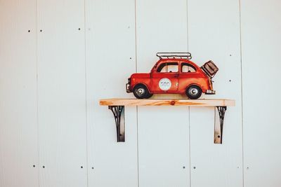 Red toy car on shelf against white wall