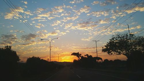 Silhouette trees by road against sky during sunset