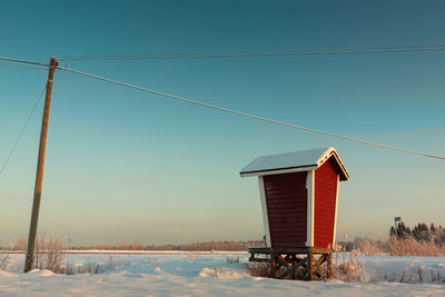 Built structure by telephone pole on snowy field against clear sky