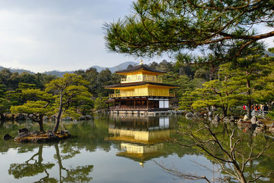 Kinkaku-ji temple by trees with reflection in pond against sky