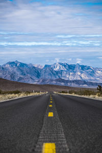 Road leading towards mountains against blue sky