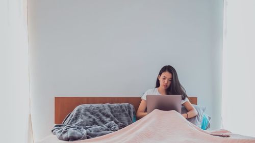 Young woman looking away while sitting on bed