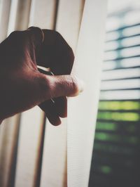 Close-up of hand holding curtain by window at home