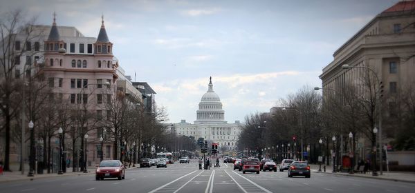 Cars moving on road leading towards united states capitol against sky in city