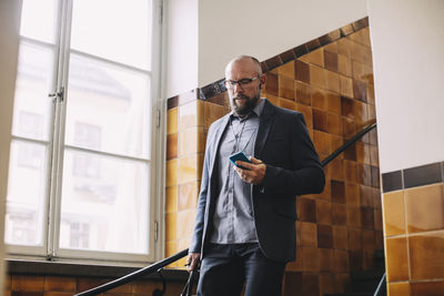 Mature businessman listening music through mobile phone while moving down steps in office