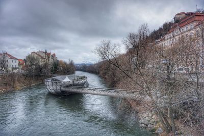 River amidst bare trees against sky in city