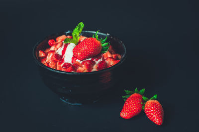 Close-up of strawberries in bowl on table against black background
