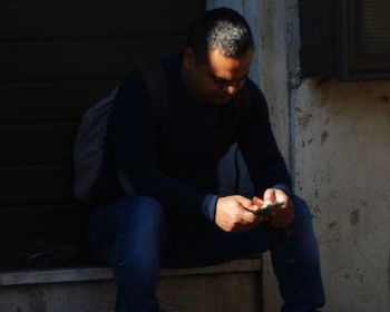 Man using mobile phone while sitting on wall