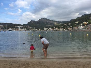 Rear view of father and daughter on beach against sky