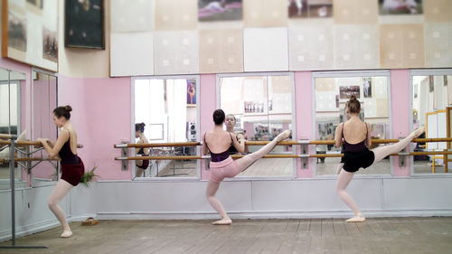 In dancing hall, young ballerinas in black leotards stretching at barre, on pointe shoes, elegantly