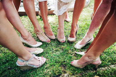 Low section of bridesmaids wearing sandals standing on grassy field