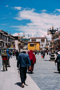 People walking on road against cloudy sky