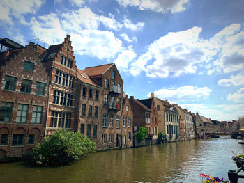 Canal by buildings in city against sky