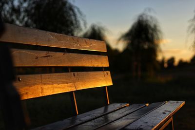 Close-up of empty bench on field against sky at sunset