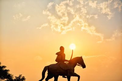 Low angle view of silhouette man sitting against sky during sunset