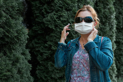 Portrait of woman wearing mask standing against trees