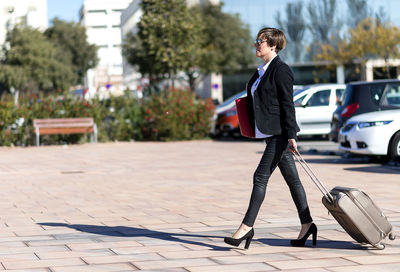 Full length of businesswoman holding suitcase walking outdoors