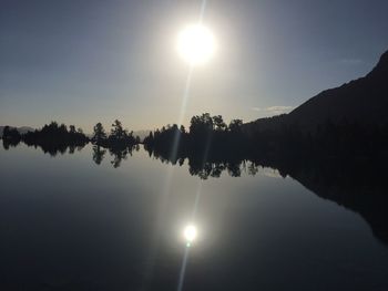 Sun shining over lake against clear sky during sunset