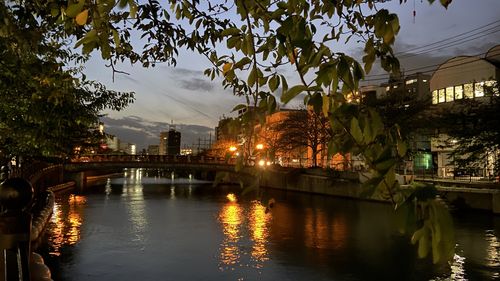 Illuminated bridge over river in city against sky