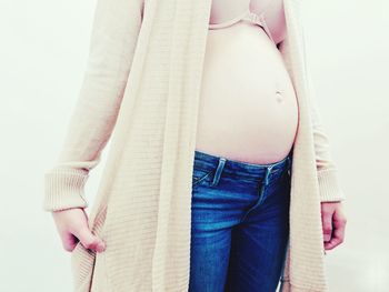 Midsection of pregnant woman wearing long coat against white background