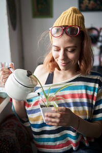 Content female in fancy clothes standing in living room and watering plant in flowerpot