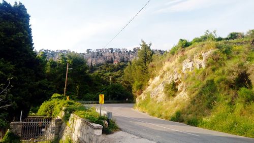 Road amidst trees and buildings against sky