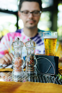 Close-up of salt and pepper shaker on table against man