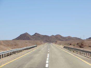 Empty road by mountains against clear sky