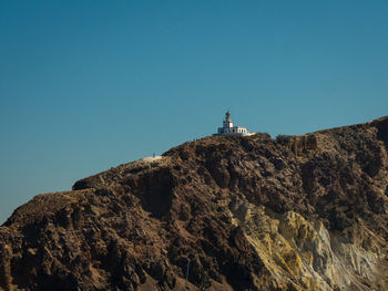 Low angle view of lighthouse on mountain against clear blue sky