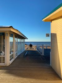 Wooden building by sea against clear blue sky