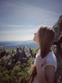 Woman standing on rock looking at mountain against sky