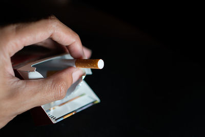 Cropped hand of person holding electronic cigarette against black background