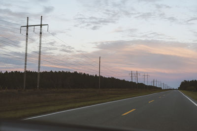 Road by electricity pylon against sky during sunset