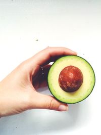 Close-up of cropped hand holding fruit over white background