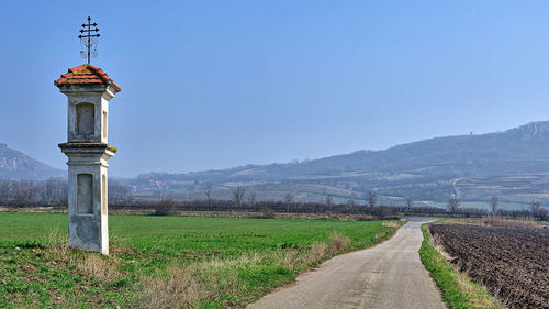 Road amidst field against clear blue sky