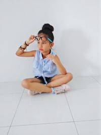 Thoughtful girl wearing eyeglasses while sitting on tiled floor