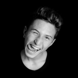 Portrait of happy teenage boy making face against black background