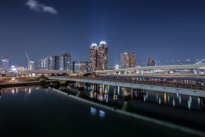 Illuminated bridge by buildings against sky at night