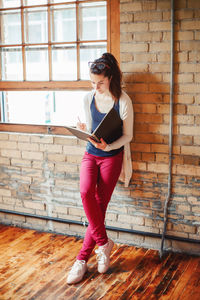 Woman drawing in book while standing by wall