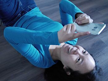 High angle view of woman using phone while lying on hardwood floor